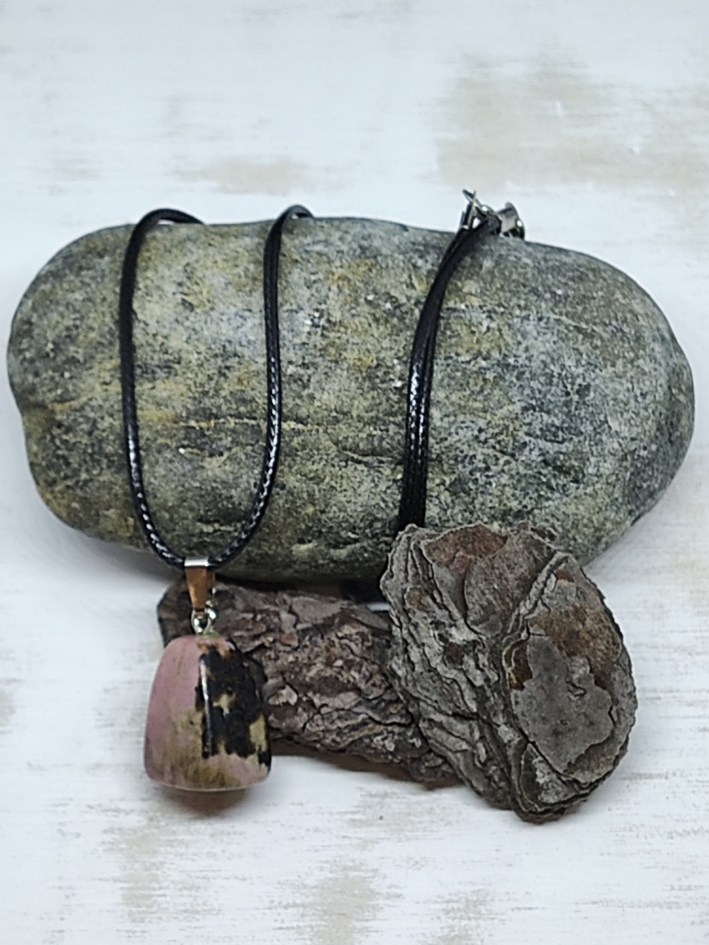 Colar com pendente de pedra rosada e cordão preto sobre pedra cinzenta e casca seca