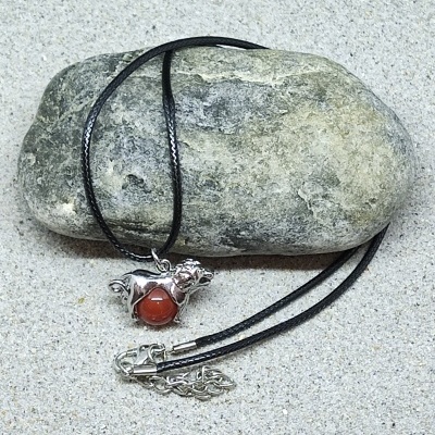 Colar com pendente de cão metálico e pedra vermelha sobre pedra cinza e areia