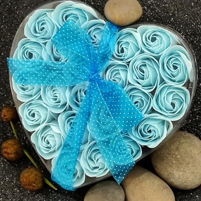 Caixa coração com flores artificiais azuis e laço azul, rodeada por pedras e flores secas