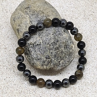 Pulseira elástica com contas pretas, cinzentas metálicas e castanhas sobre pedra cinzenta em areia clara