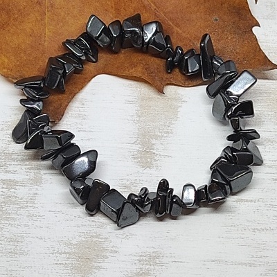 Pulseira de pedras pretas polidas sobre superfície branca com folha seca castanha ao fundo