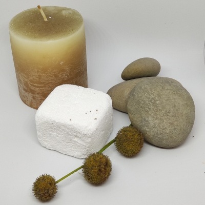 Conjunto decorativo com vela marfim, pedras cinza, bloco branco e ramo com frutos secos castanhos