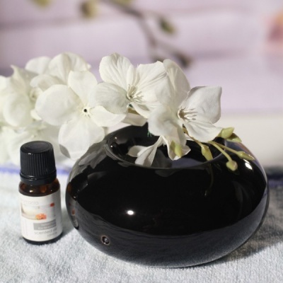 Difusor de aroma preto arredondado com flores artificiais brancas e frasco de óleo essencial