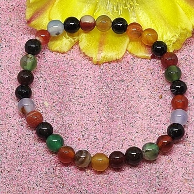 Pulseira colorida com contas redondas sobre fundo rosa e flor amarela