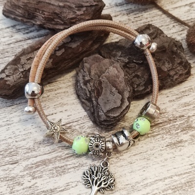 Pulseira com pingentes metálicos e miçangas verdes sobre superfície clara com madeira