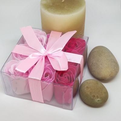 Caixa transparente com flores de sabão rosa, vela bege e duas pedras