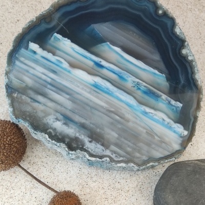Fatia de ágata azul sobre superfície clara com flores secas e pedra cinza
