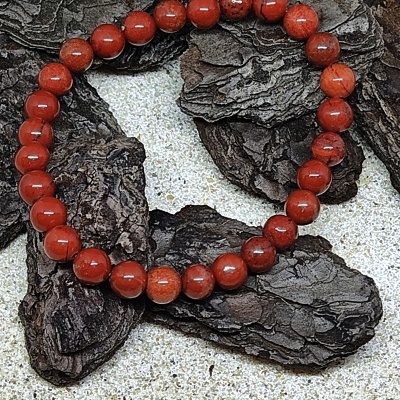 Pulseira elástica de contas de madeira castanho avermelhado sobre cascas de árvore secas.