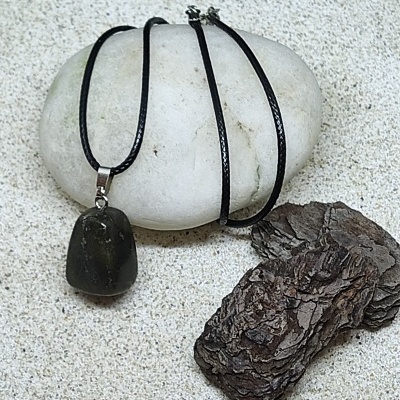 Colar com pendente de pedra preta sobre pedra branca e casca de árvore na areia