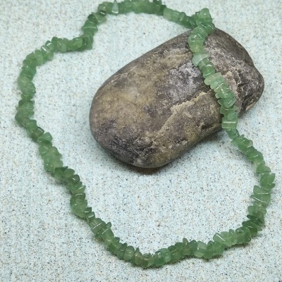 Colar de pedras verdes sobre superfície clara ao lado de pedra maior