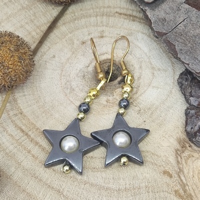 Brincos estrela cinza com pérola e contas douradas sobre madeira