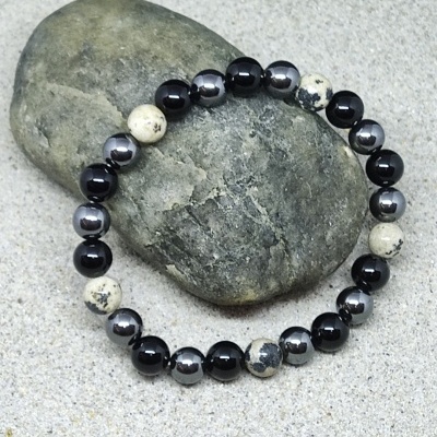 Pulseira de contas pretas, cinzentas e bege sobre pedra cinza