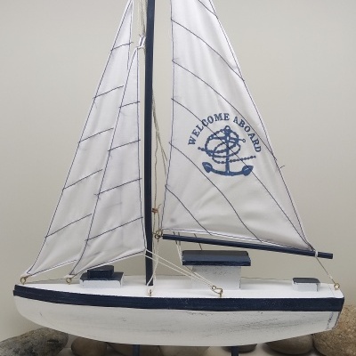 Barco decorativo de madeira branco e azul com velas brancas e texto 'WELCOME ABOARD'
