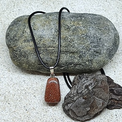 Colar com pendente de pedra castanha brilhante e cordão preto sobre pedra cinzenta