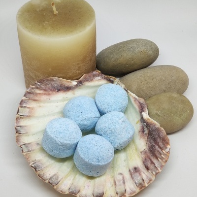 Pastilhas azuis em concha natural com vela amarela e pedras cinzentas