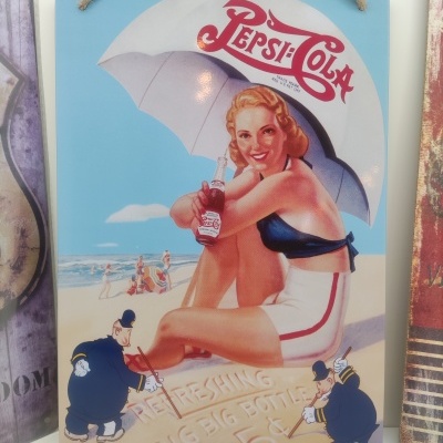 Placa metálica vintage com mulher na praia segurando garrafa de Pepsi-Cola sob guarda-sol
