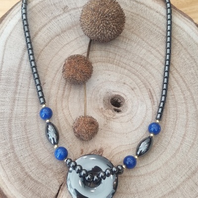 Colar com contas metálicas prata e azuis e peça central redonda sobre madeira