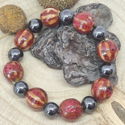 Pulseira com contas laranja avermelhadas e negras sobre madeira clara