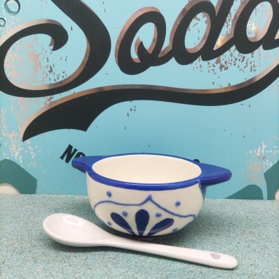 Tigela de cerâmica branca e azul com colher branca em superfície azul clara e fundo com texto 'Soda'