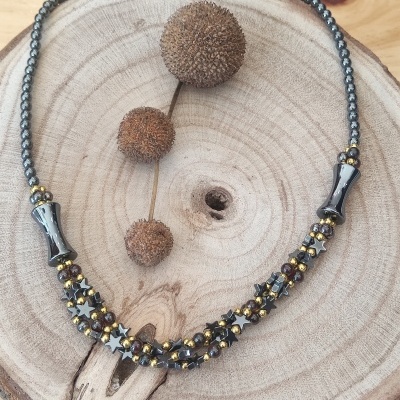 Colar com contas metálicas cinzentas e douradas sobre base de madeira com sementes secas