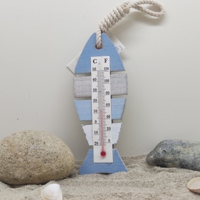 Termómetro decorativo em forma de peixe em madeira azul e branca com corda, na areia entre pedras e conchas
