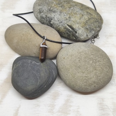 Colar com pendente castanho em pedra e metal sobre pedras naturais de vários tons