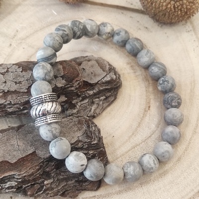 Pulseira de contas cinza marmorizadas com detalhes prateados sobre madeira