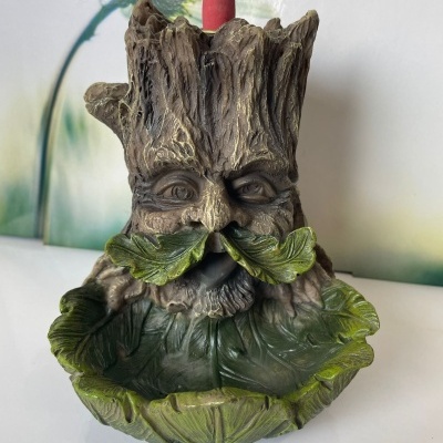 Incensário de tronco de árvore com rosto e folhas verdes, cone de incenso vermelho no topo