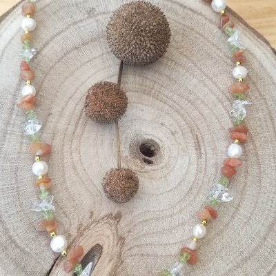 Colar colorido com pedras e pérolas sobre suporte de madeira redonda com frutos secos