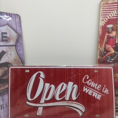 Placa vermelha decorativa com texto 'Open Come in WE'RE' em branco