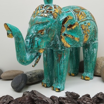 Escultura de elefante verde e dourado em madeira com pedras e cascas ao redor