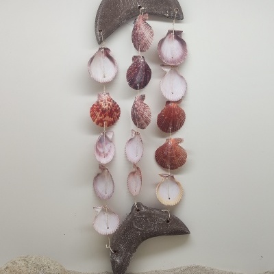 Móbile decorativo de conchas naturais pendurado com peças de madeira e areia ao fundo