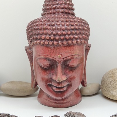 Estátua da cabeça de Buda vermelha com textura em relevo e pedras decorativas ao redor