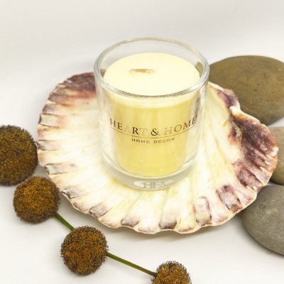 Vela amarela clara em copo de vidro com texto sobre concha e pedras com bolas secas marrons