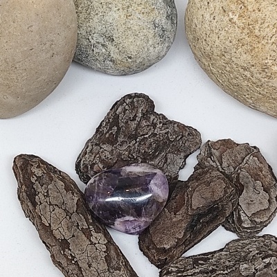 Pedra polida roxa sobre cascas de árvore e pedras maiores arredondadas