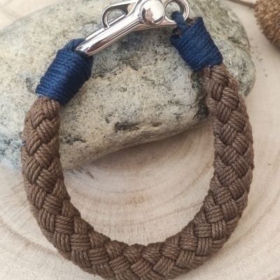 Pulseira de corda marrom trançada com fecho metálico e detalhes em azul escuro sobre pedra