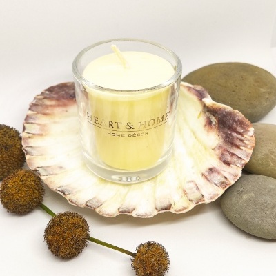 Vela amarela em copo de vidro sobre concha marrom e branca com pedras cinza e bolas secas castanhas