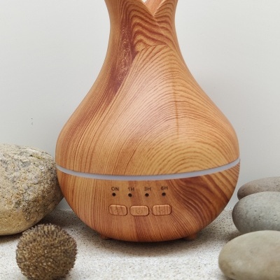 Difusor de aroma em madeira clara com botões e indicações de tempo, rodeado por pedras.
