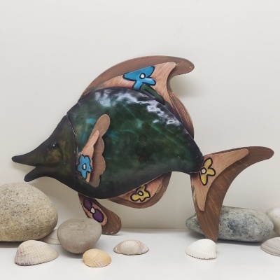 Peixe decorativo em madeira e metal com flores coloridas rodeado por pedras e conchas.