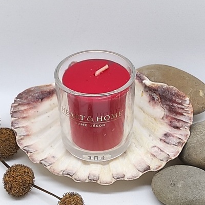 Vela vermelha em recipiente de vidro sobre concha com pedras e ramos secos