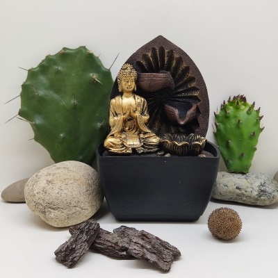 Fonte decorativa preta com estátua dourada de Buda entre pedras e cactos