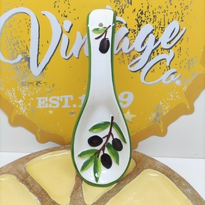 Colher de cerâmica branca decorada com azeitonas em fundo amarelo