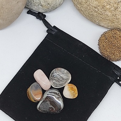 Cinco pedras polidas coloridas sobre saco preto com pedras maiores ao fundo