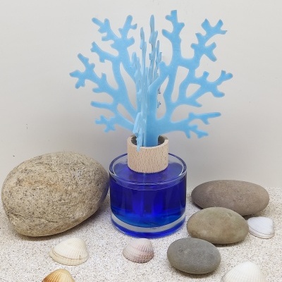 Frasco azul com paus decorativos azuis, pedras e conchas em areia