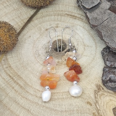 Brincos com pedras laranja e pérolas sobre madeira clara e casca escura