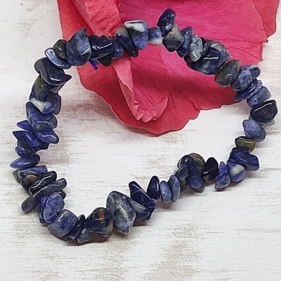 Pulseira de pedras azuis sobre superfície branca com flor rosa ao fundo