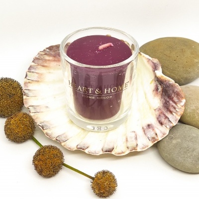Vela roxa em copo de vidro com inscrição 'HEART & HOME' sobre concha com bolas secas e pedras