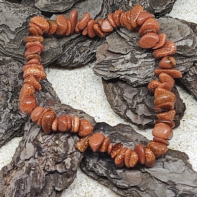 Pulseira de pedras castanho-avermelhadas com brilho dourado sobre cascas de árvore