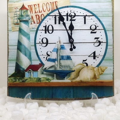 Relógio decorativo com tema náutico, incluindo farol, barco à vela, conchas e texto de boas-vindas.