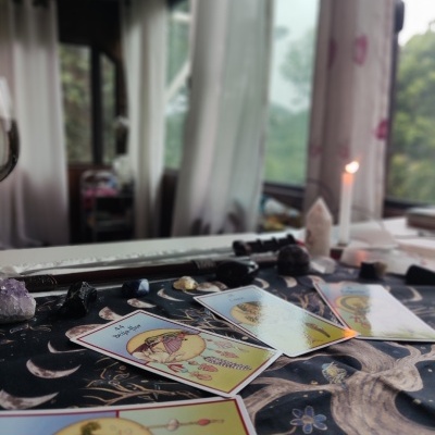 Cartas de oráculo sobre tecido com padrões lunares e pedras com vela ao fundo